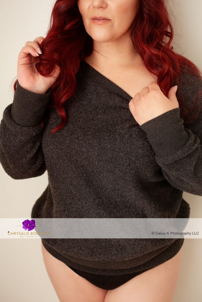 Curly Red Head single mom building confidence wearing grey sweatshirt standing against wall for Boudoir Photoshoot