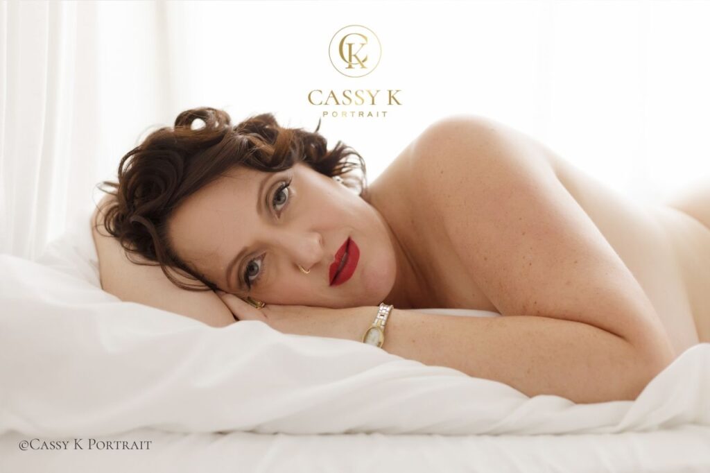 Brunette Blue eyed woman laying on bed with body confidence white sheet boudoir photography