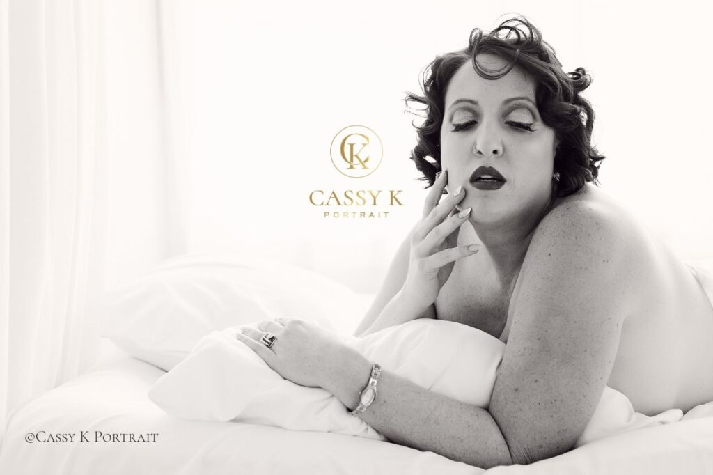 Brunette Blue eyed red lipped woman laying on bed with body confidence white sheet boudoir photography