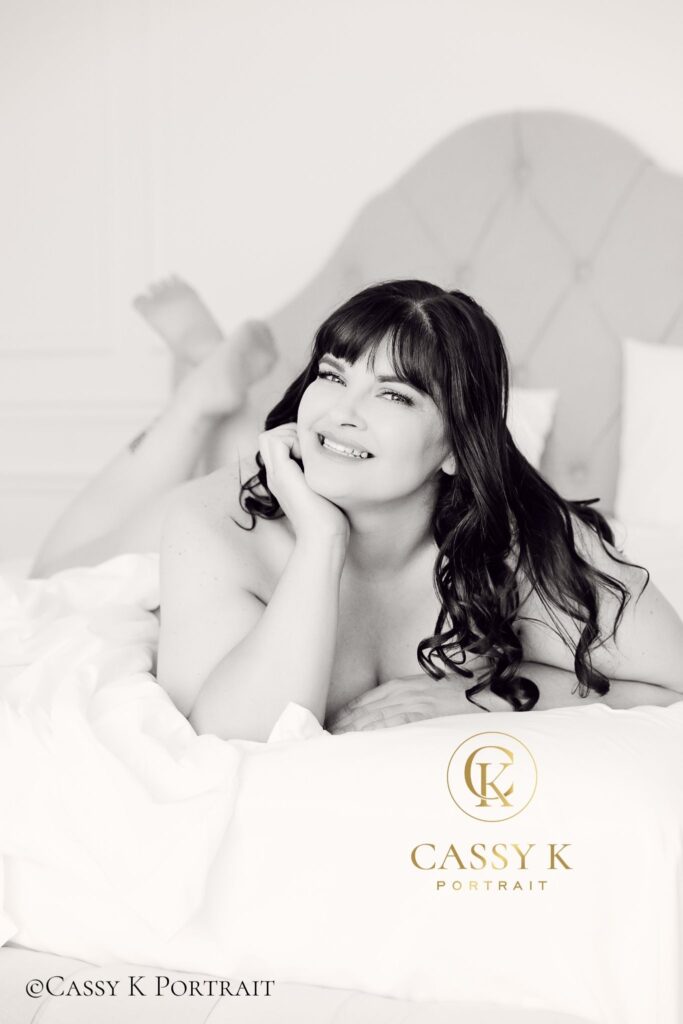 Brunette hair and green eyed woman investing in self love during white sheet black and white Boudoir Photoshoot