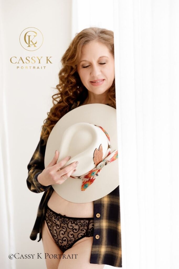 Busy business owner experiences confidence boost through showing her authentic style by wearing black lace, panama hat with feather, and flannel during boudoir photo shoot