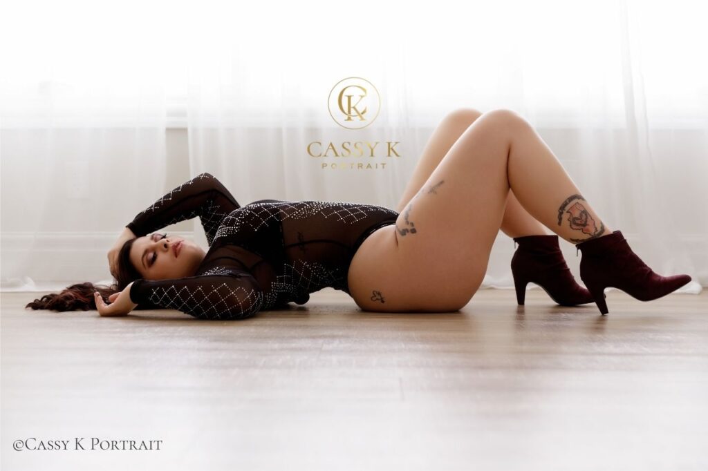 Young woman wearing black sheer and rhinestone bodysuit works through body changes and falls in love with herself for the first time during boudoir photo shoot