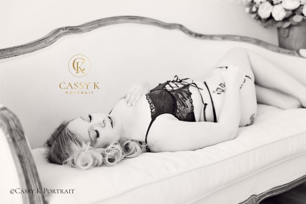 A stunning black and white portrait of a woman reclining in lace lingerie on a vintage sofa during her luxury elevated boudoir experience.