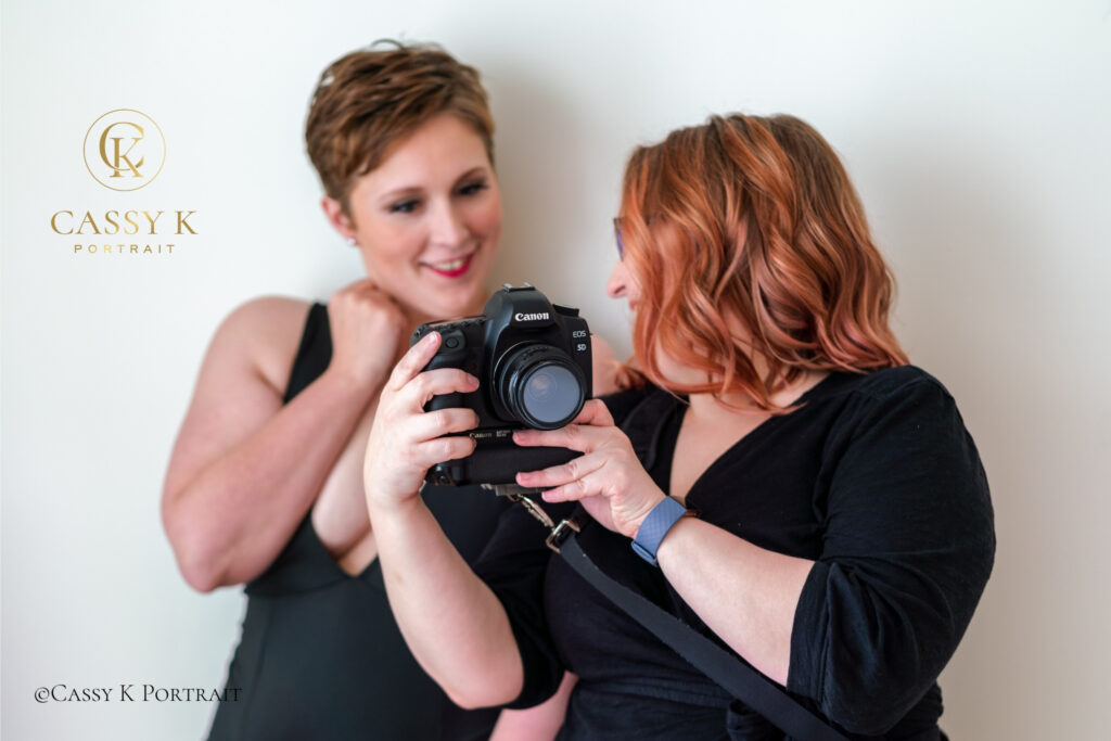 A woman and her portrait photographer smile as they review an image together on the back of the camera.